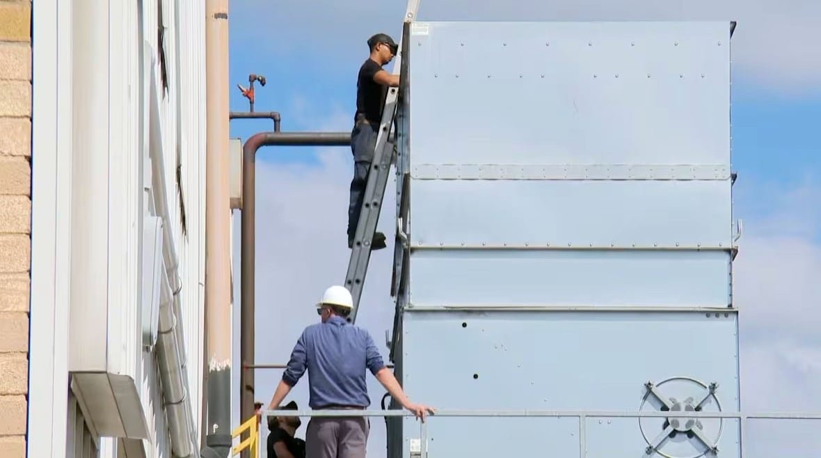 One person stands on a ladder looking into a cooling tower as another stands below.