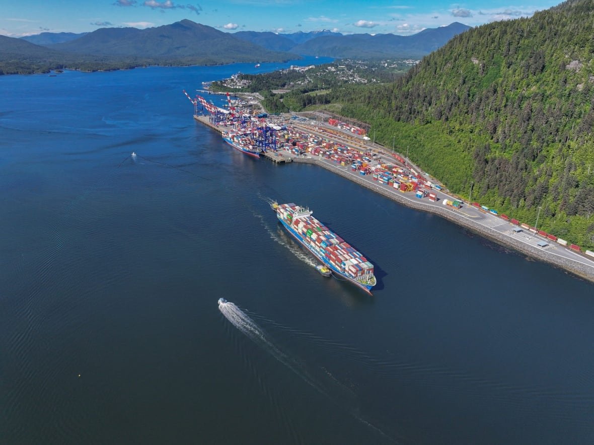 A drone shot of a big ship carrying cargo in the ocean with a terminal in the background.