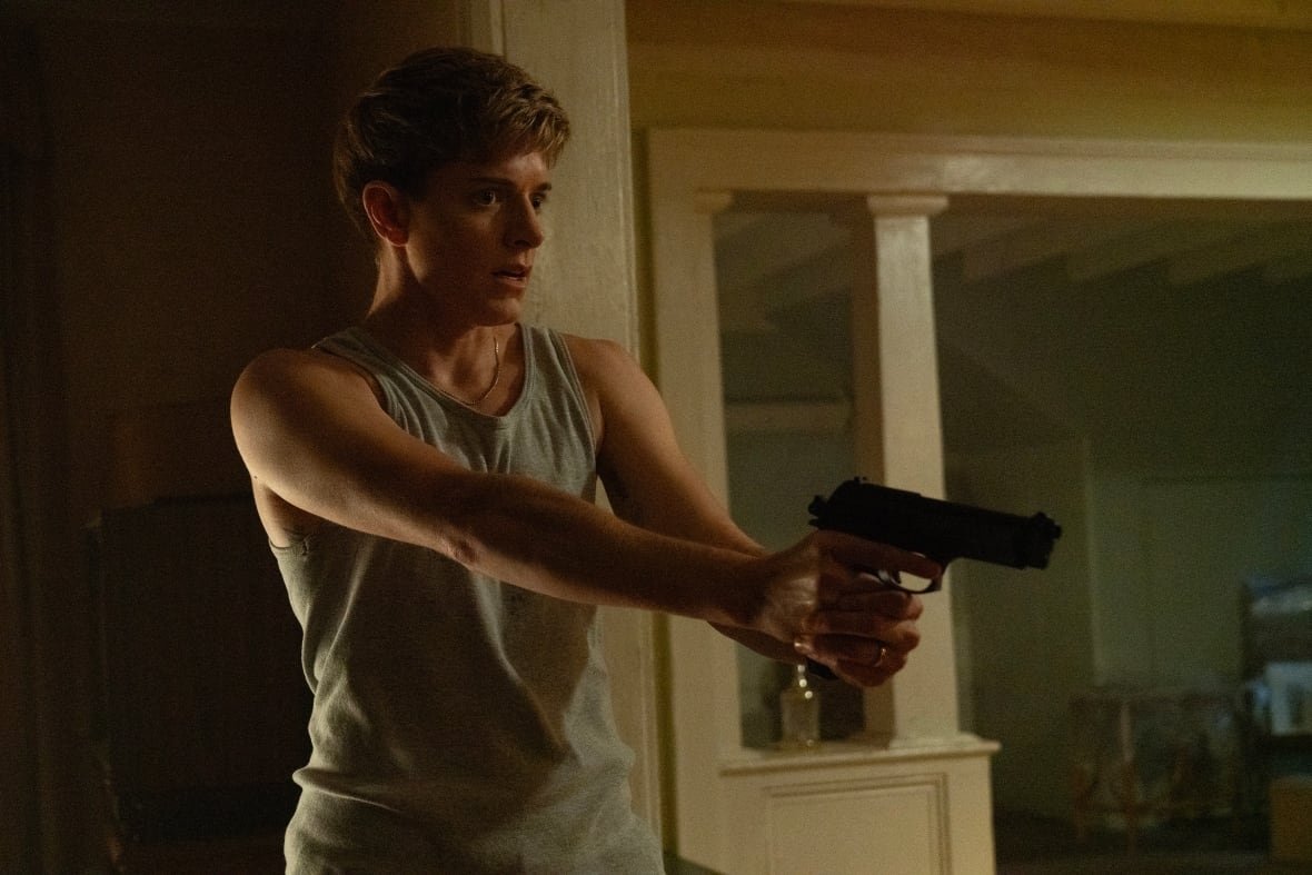 A person in a tank-top holds a gun.