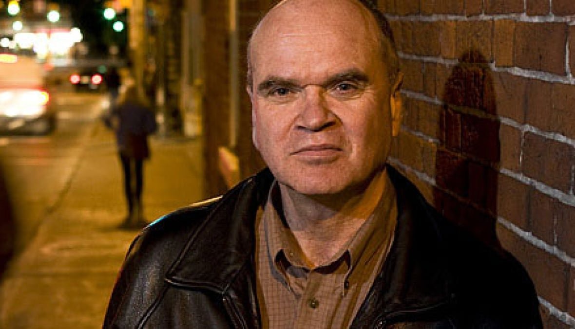 A man stands on the sidewalk next to a brick wall.