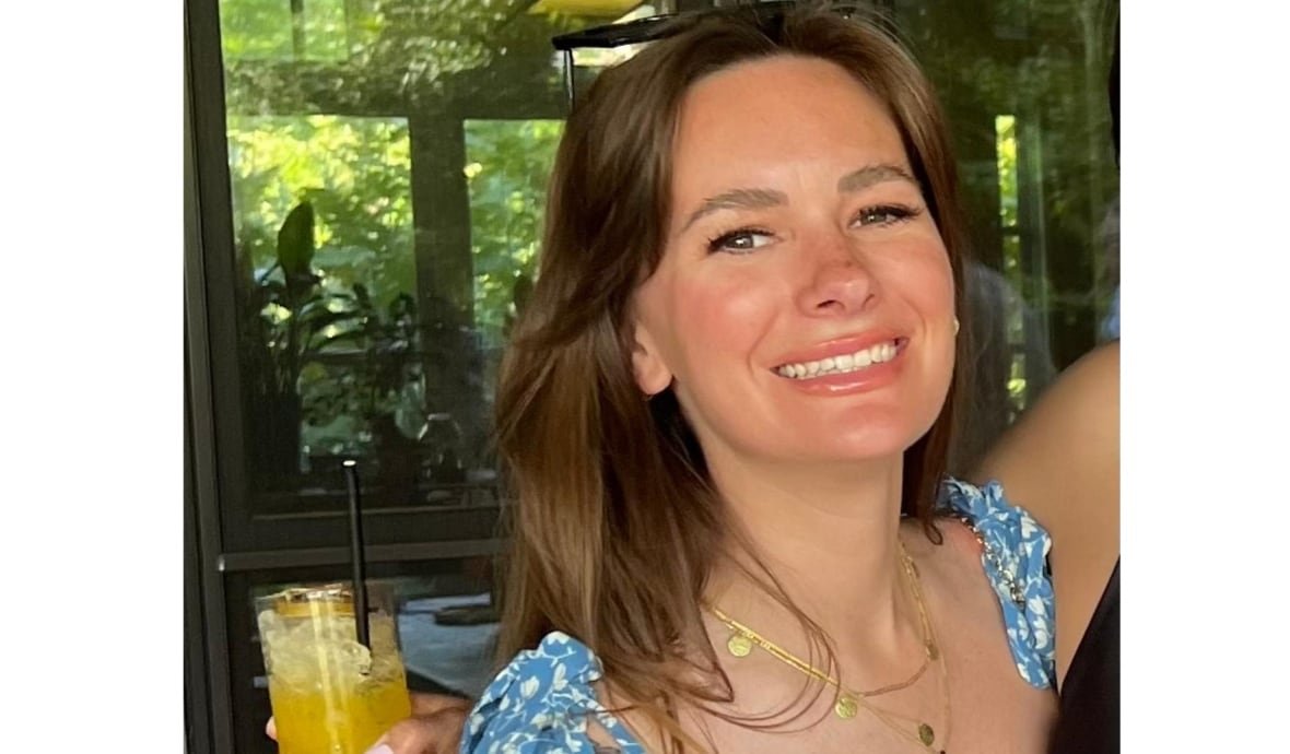 A woman with long brown hair wearing a blue and white sundress smiles at the camera.