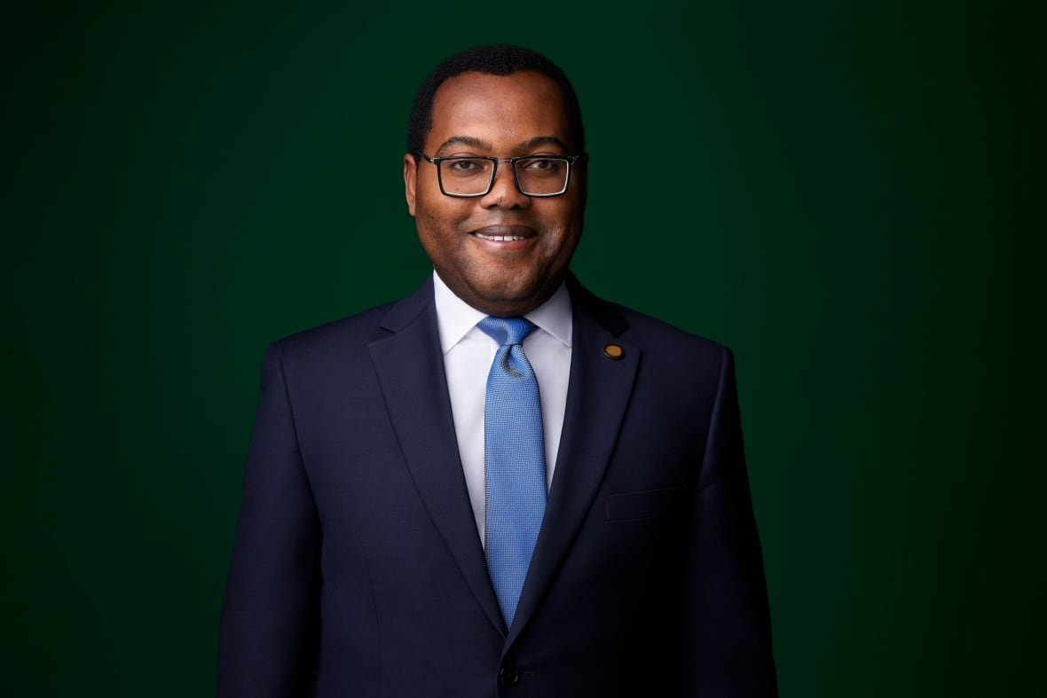A portrait of a smiling man in glasses, a dark suit and light blue tie.