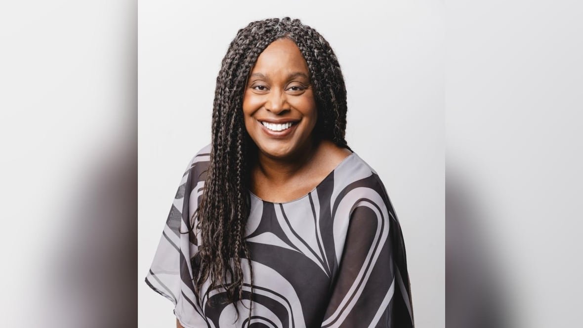 A portrait of a smiling woman with long braided hair and a black and grey blouse.