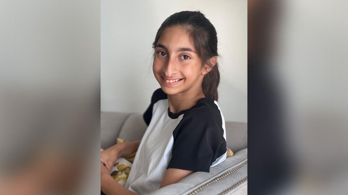 A portrait of a smiling girl in a black and white t-shirt sitting on a grey couch.
