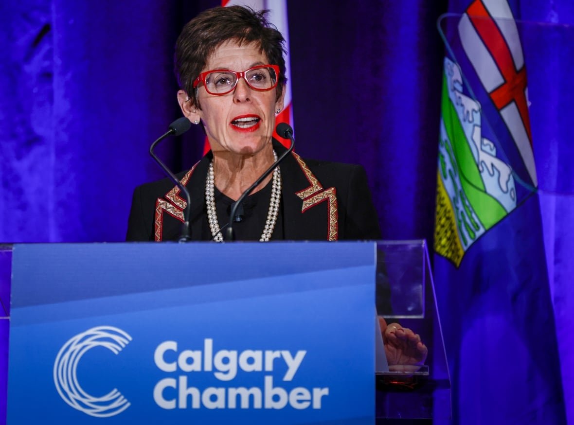A woman wearing glasses is pictured behind a podium.