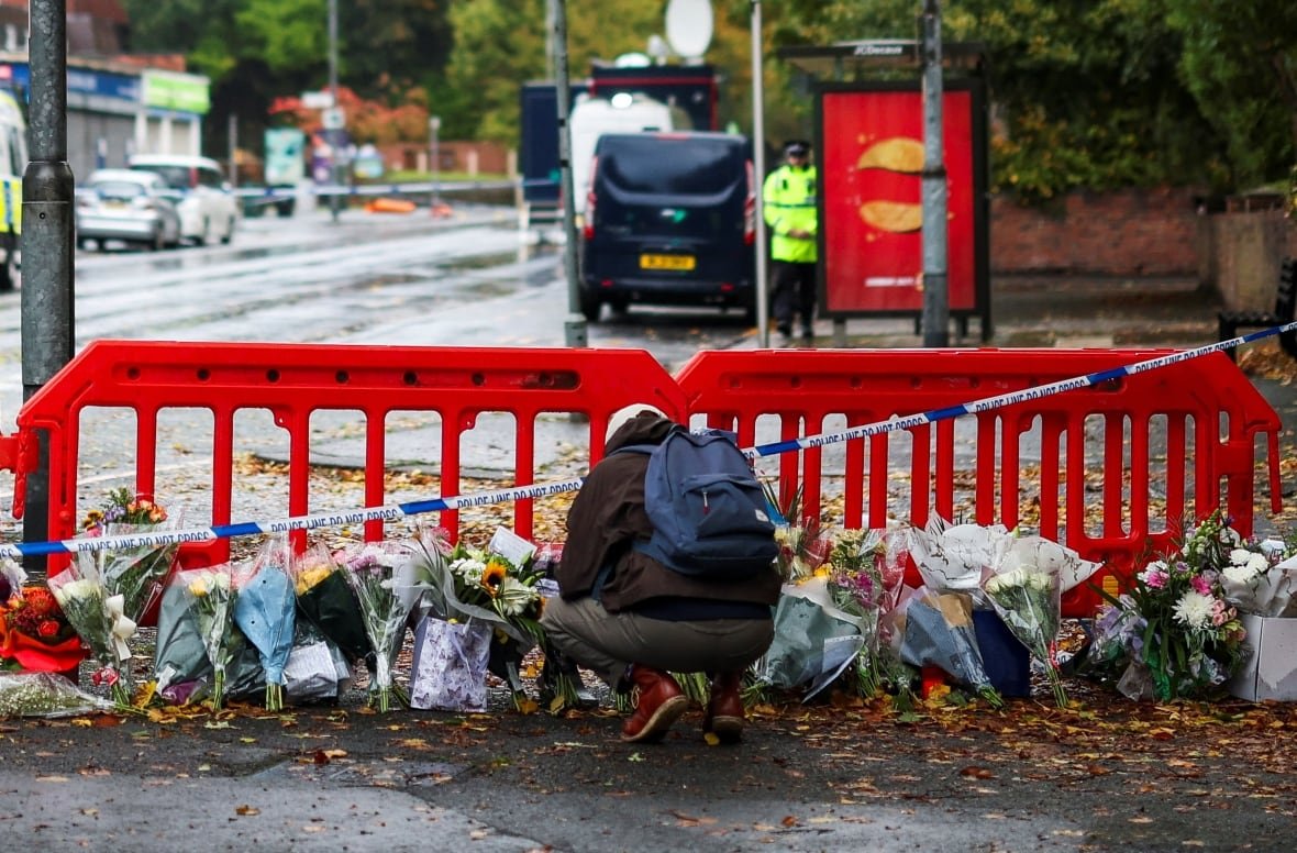 A person crouches next to floral tributes left near the Manchester synagogue, where multiple people were killed on Yom Kippur, in what police have declared a terrorist incident, in north Manchester, Britain, October 4, 2025.