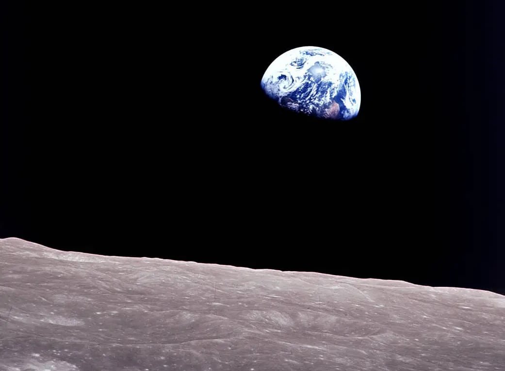 The earth seen in the distance against a black background, the moon's surface in the foreground.
