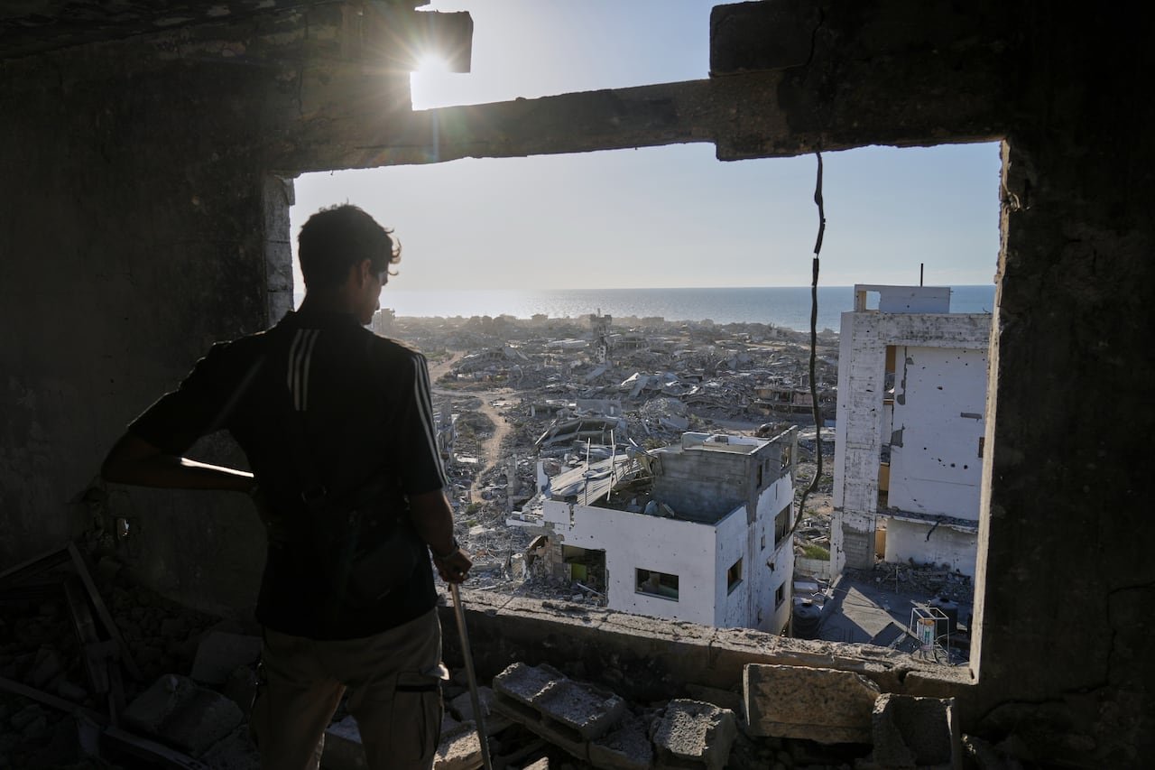 A man looks through a destroyed window overlooking a destroyed city as a ray of sun pokes through.