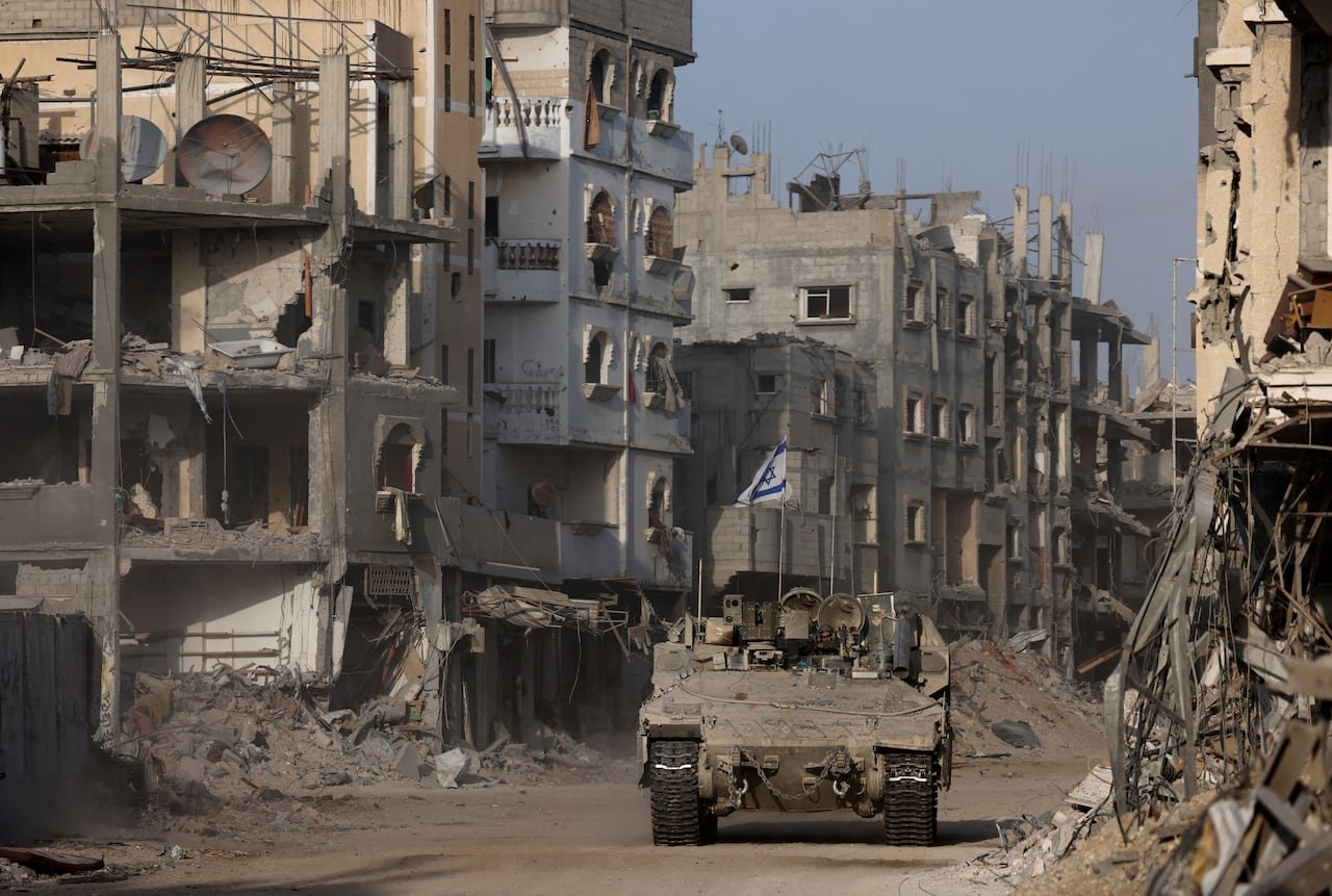 An armoured vehicle with an Israeli flag on it drives through ruins.