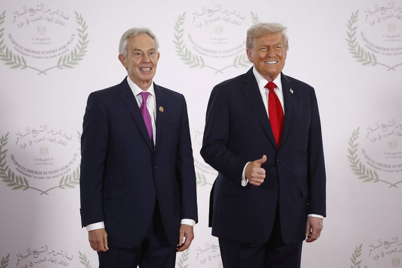 Two men in suits pose for a photo in front of a white backdrop.