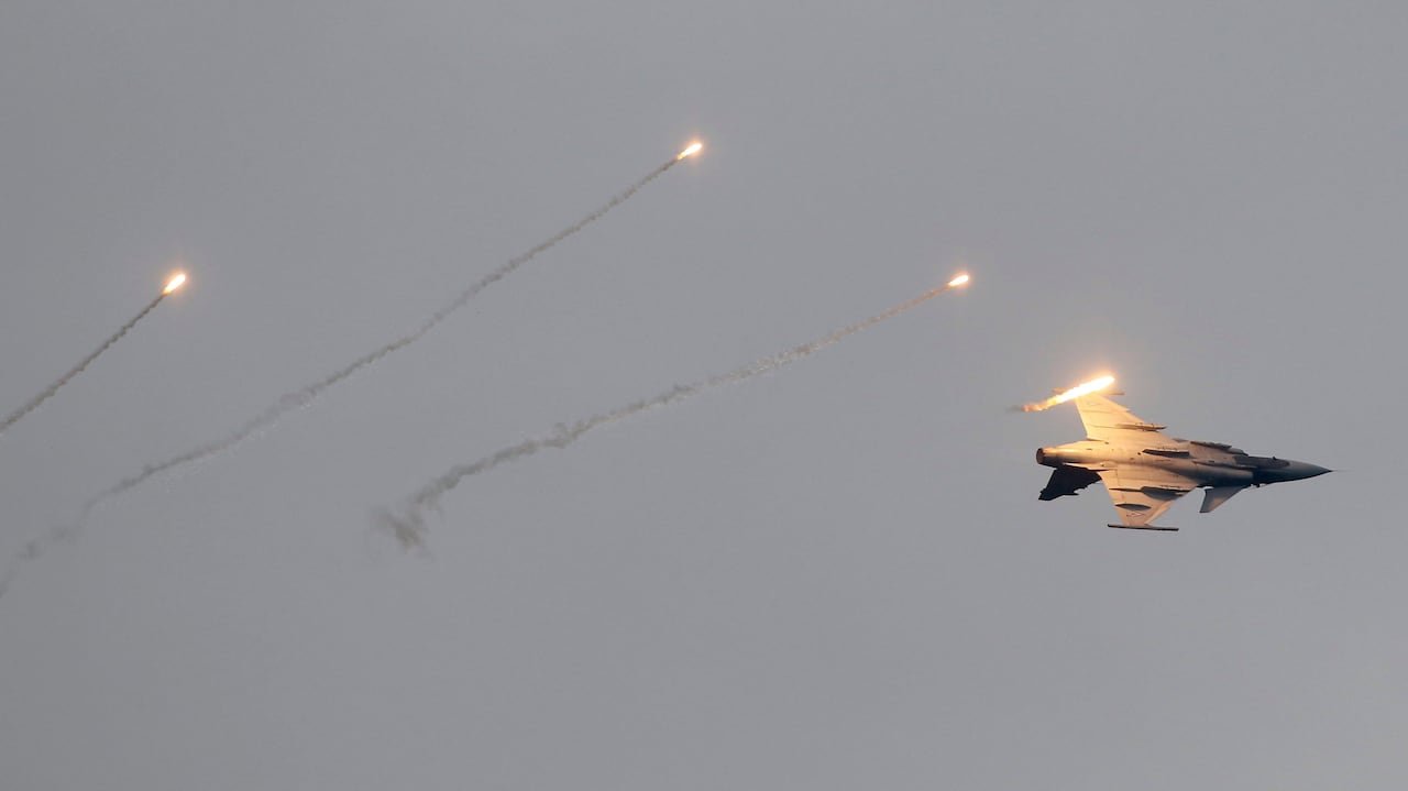 A fighter jet performs a barrell roll as flares dot the sky.