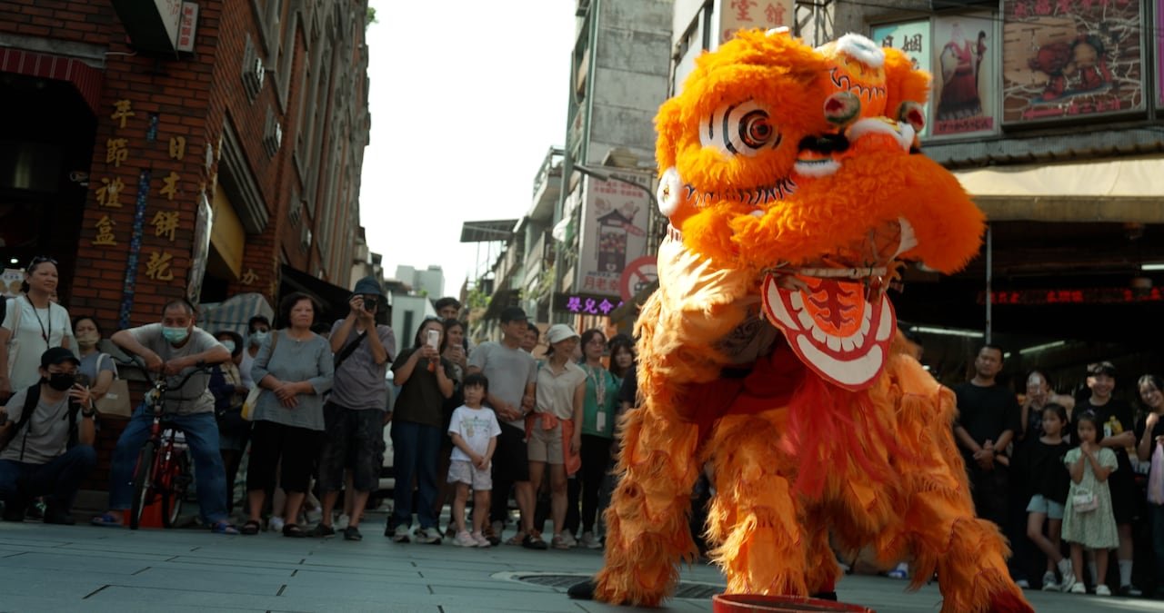 People stand outside looking at a large orange creature