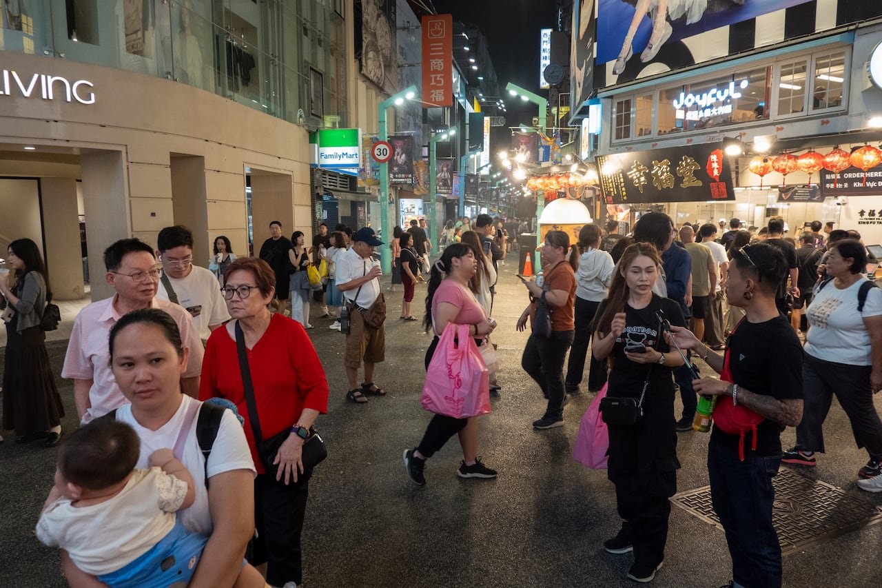 People are seen outside in a shopping district at night.