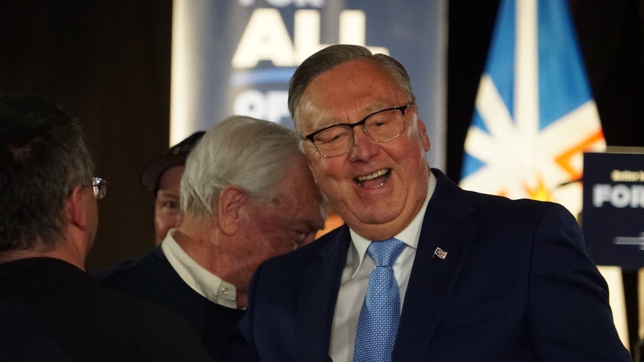 A man wearing a suit and glasses smiles widely
