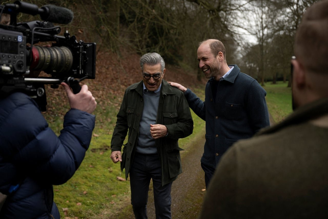 Two people walk down a path in front of a video a person operating a video camera.