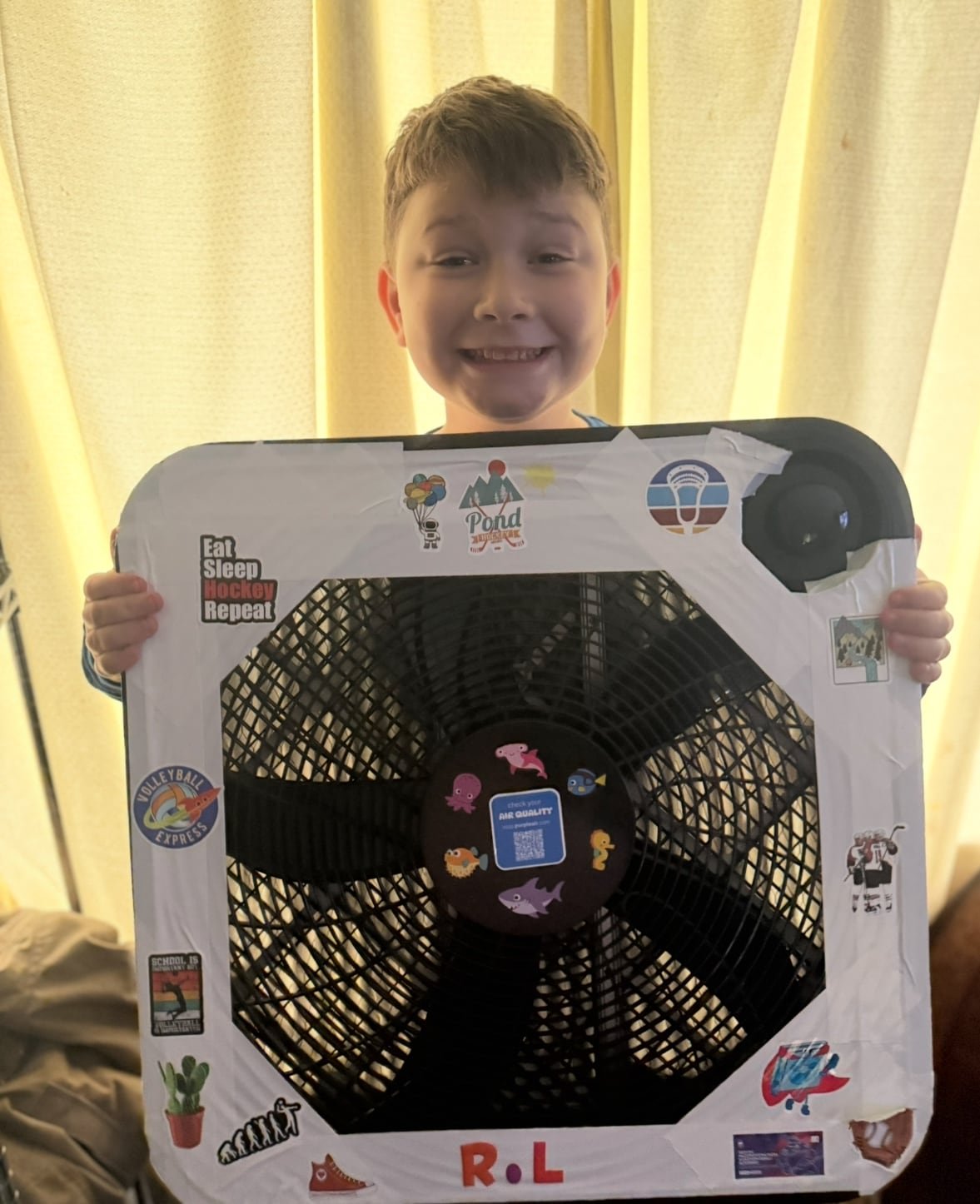 Young boy smiles holding up a homemade air quality monitor with stickers on the border