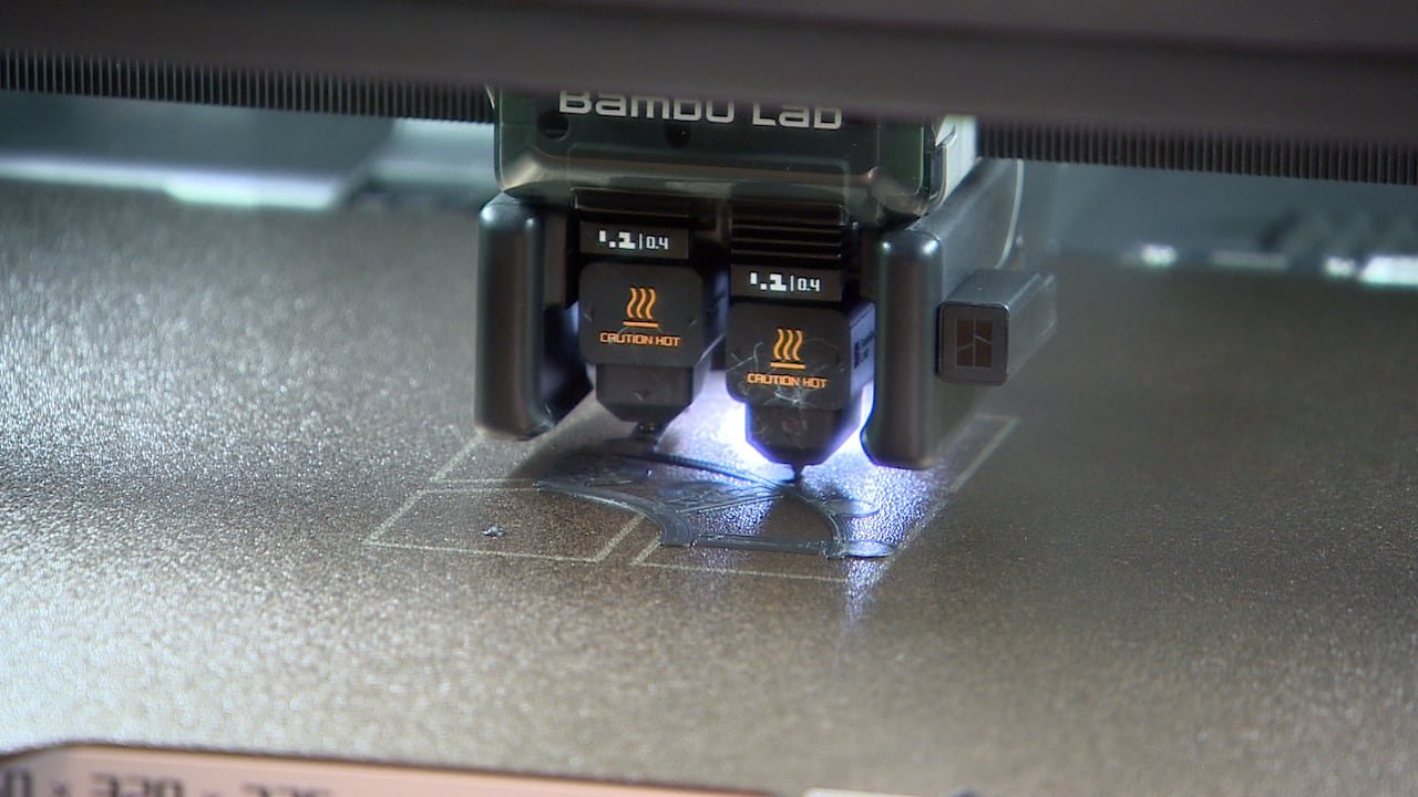 A close up of a machine that has two printer heads laying down plastic in a geometric shape.