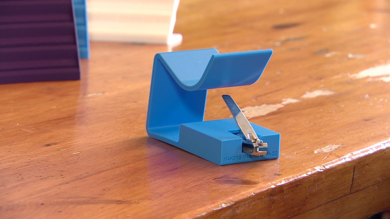A metal nail clipper rests inside a blue plastic stand that has a lever extending upward.