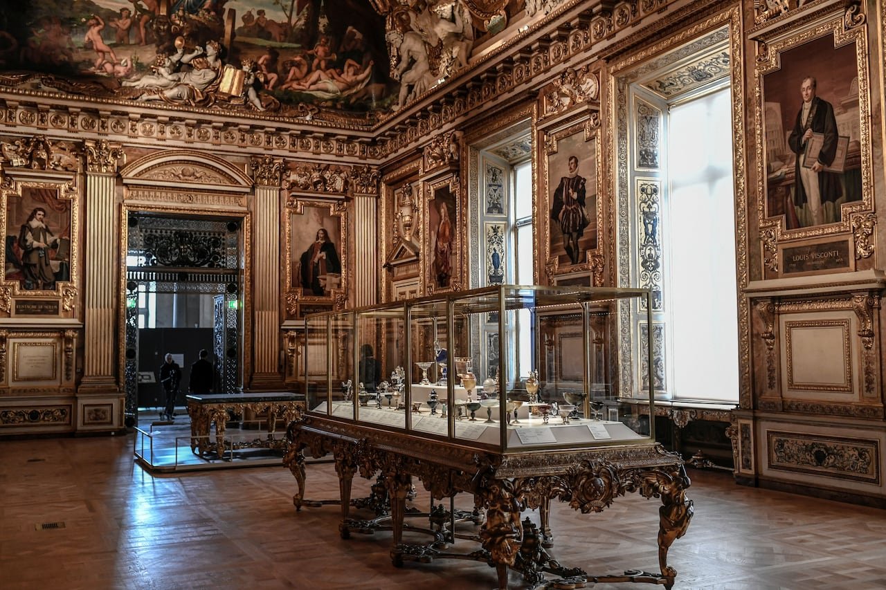 A glass case of jewelry is shown in an ornate room.