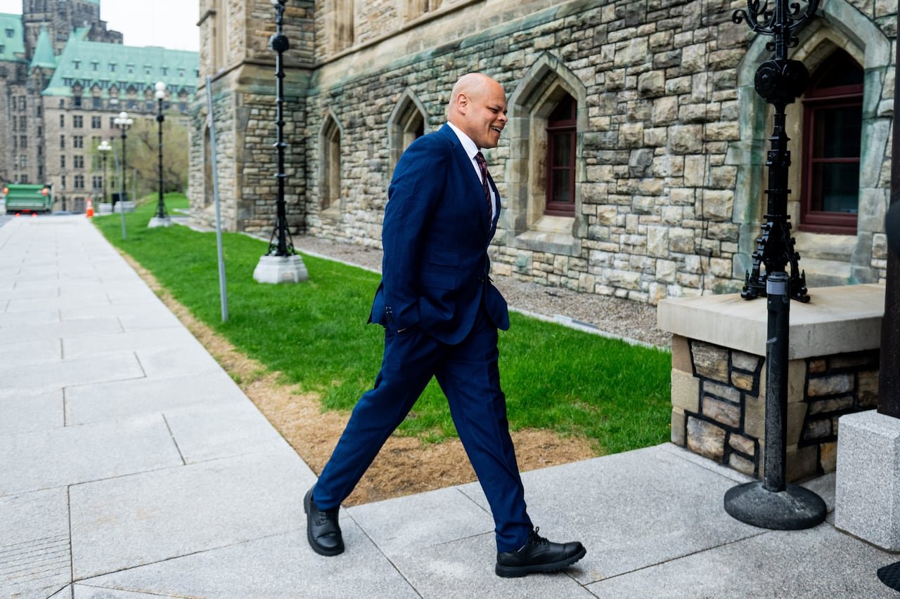 A man in a blue suit walks outdoors in front of a historic building.