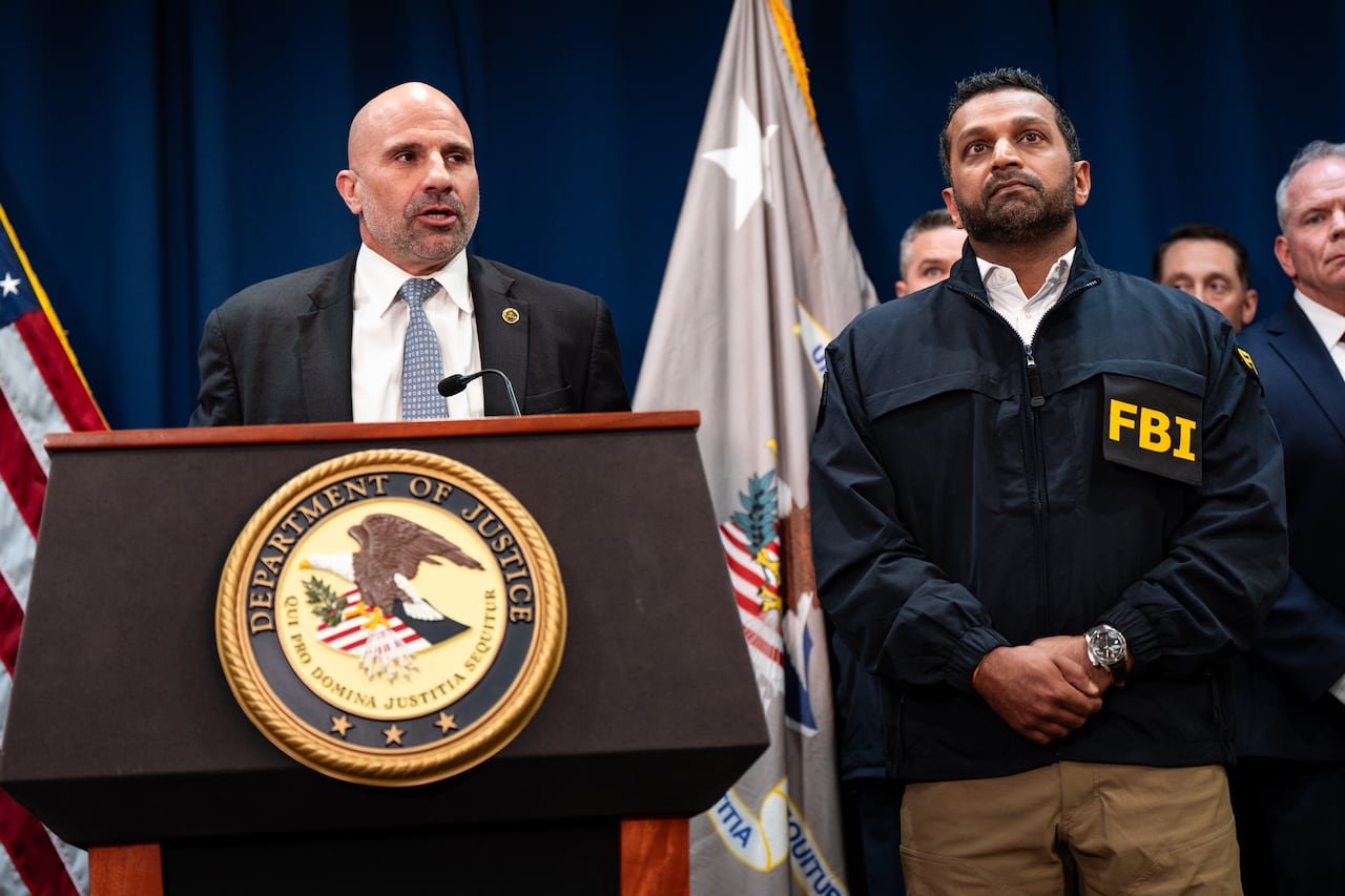 A man in a suit speaks at a podium that says US department of justice.