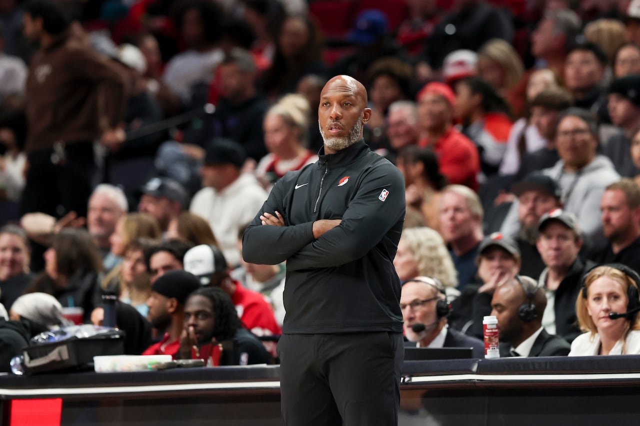 A man in a coaching uniform stands with his arms crossed