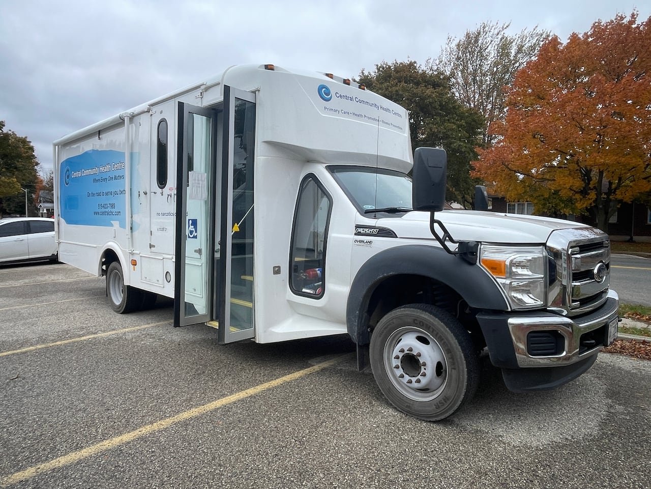 A mobile health unit on wheels parked across three spots in a church parking lot.  