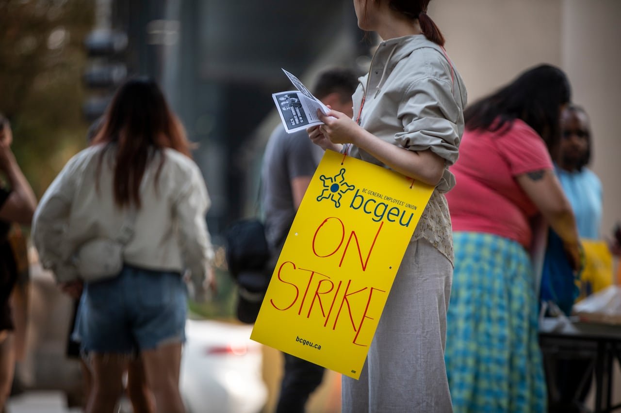 A woman holds a yellow sandwich board reading 'On Strike'.
