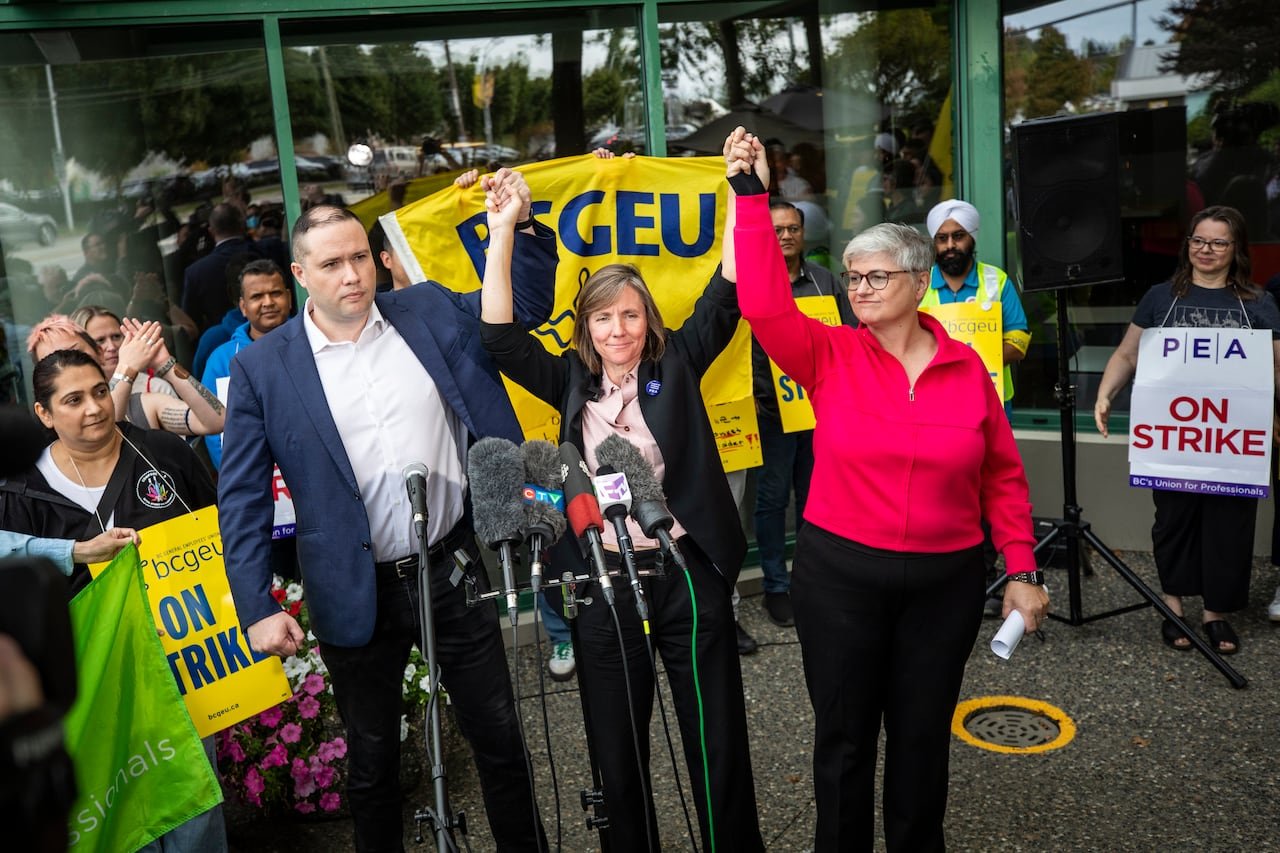 Three people hold their hands up high at a strike rally.