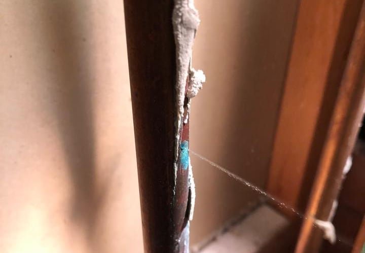 A close-up of a copper pipe with water leaking out.