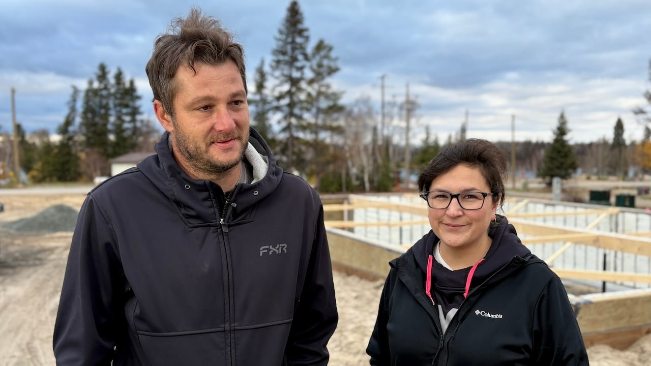 A man and woman pose for a photo outside in front of the foundation of their new house.