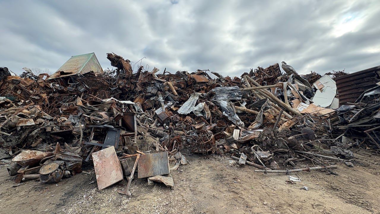 A large pile of charred, melted and twisted scrap metal at an outdoor dump.