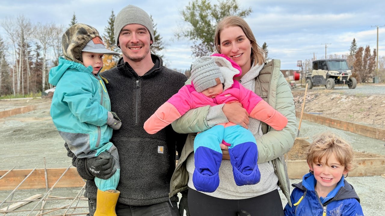 A man and woman pose with three children outside at a construction site.