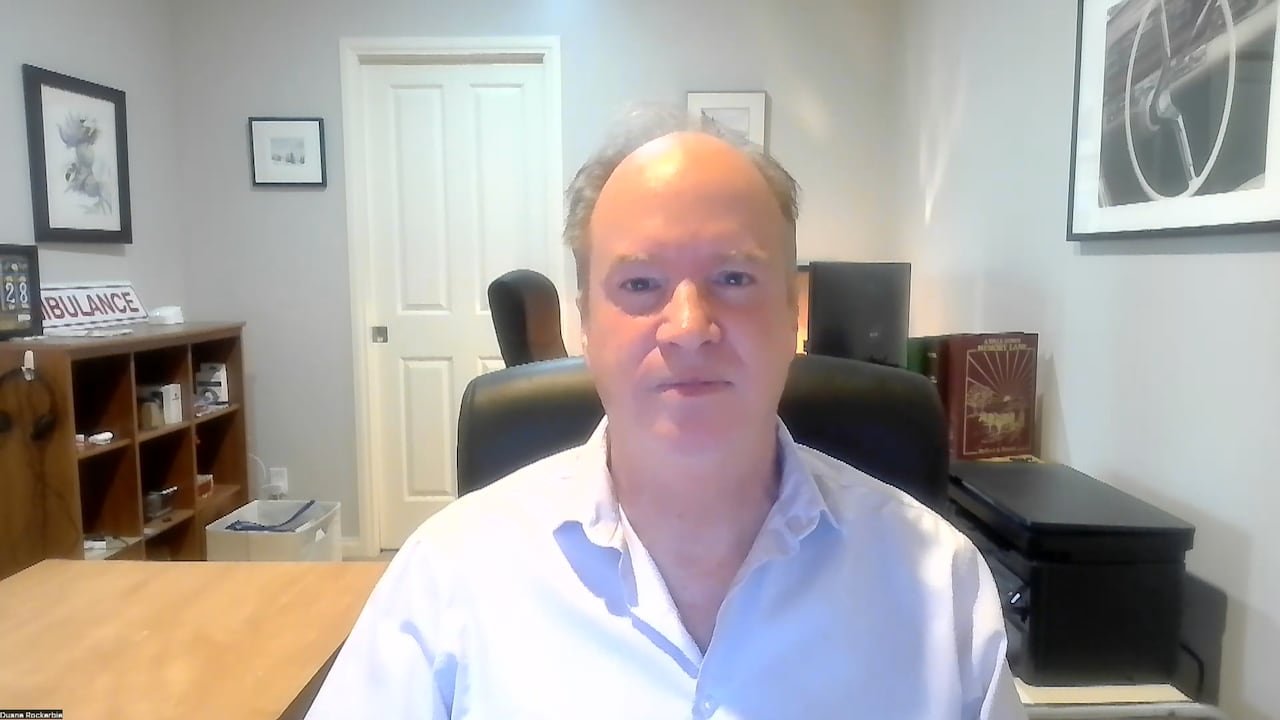 A man in a bright white shirt sitting in an office looks into the camera.