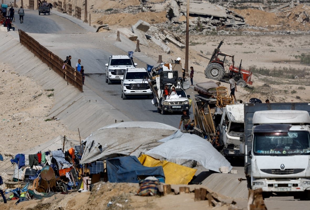 United Nations vehicles drive on a road as displaced Palestinians, fleeing northern Gaza due to an Israeli military operation, walk nearby.