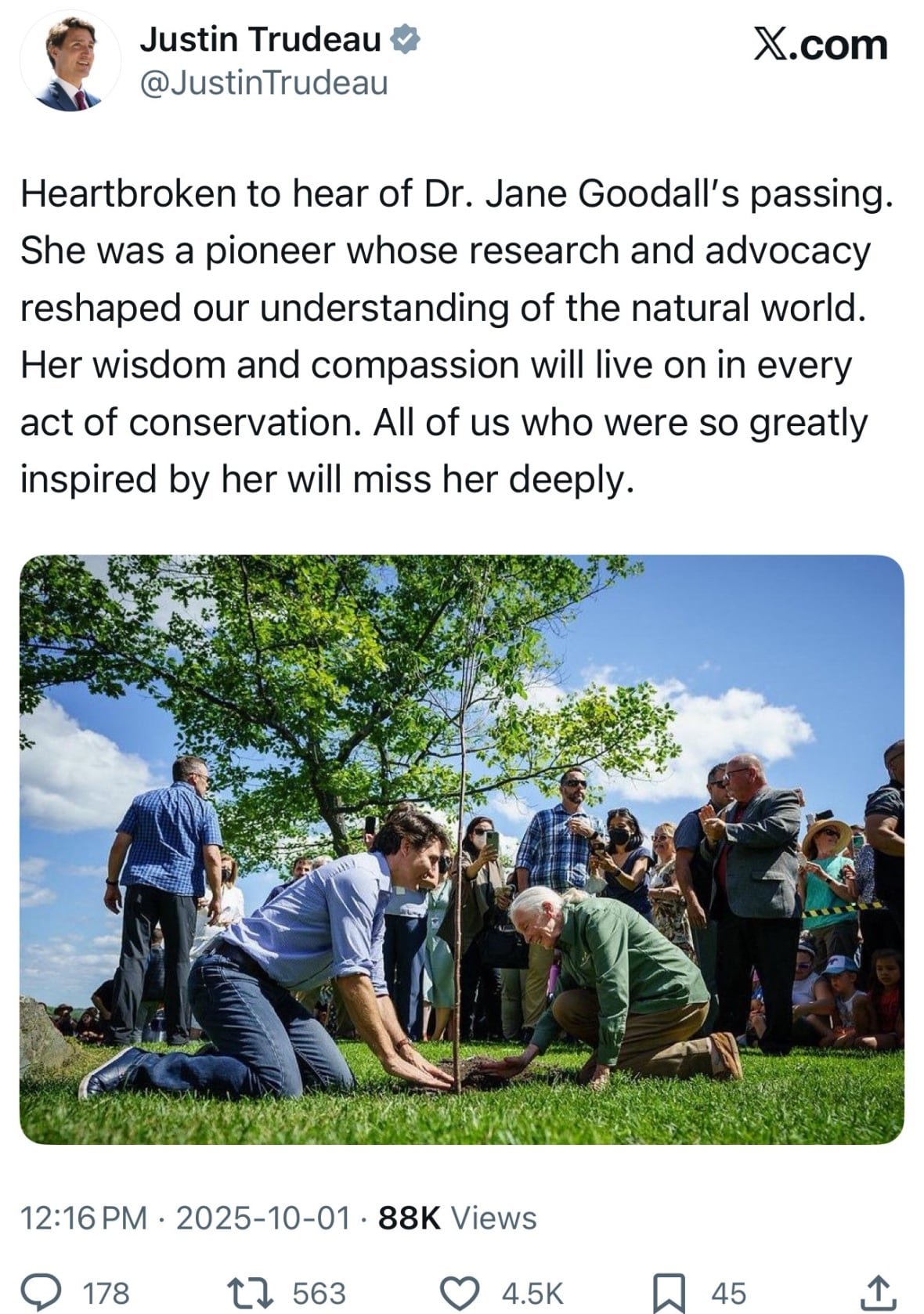 A social media post with an image of a smiling man, wearing a blue dress shirt and blue jeans on his knees on the grass planting a tree with a woman, wearing a green top and brown pants, who is smiling as she pats the dirt around the tree. A crowd stands behind them watching on a sunny, blue sky day.